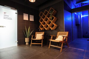 Ein Empfangsbereich mit zwei Holzstühlen, einem Blumentopf und einem an der Wand befestigten Holzregal mit Pflanzen.