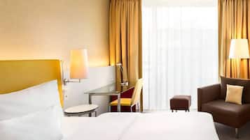 Habitación de hotel con una cama grande, un escritorio con una silla, una mesita, un sofá y una ventana con cortinas.