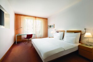Een hotelkamer met een bed, een bureau, een stoel, een televisie en een raam met gordijnen.