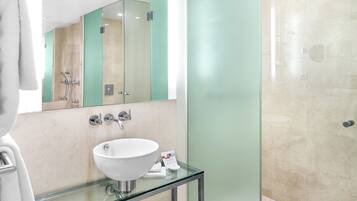 Un baño moderno con lavamanos de vidrio, cabina de ducha de vidrio y bañera blanca.