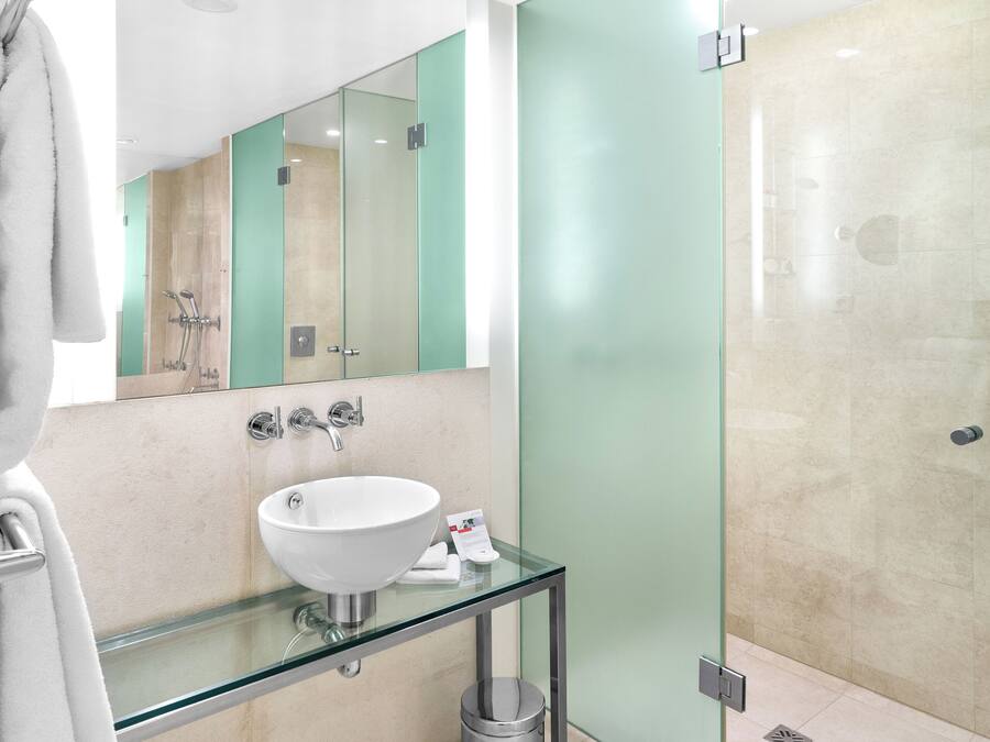 Un baño moderno con lavamanos de vidrio, cabina de ducha de vidrio y bañera blanca.