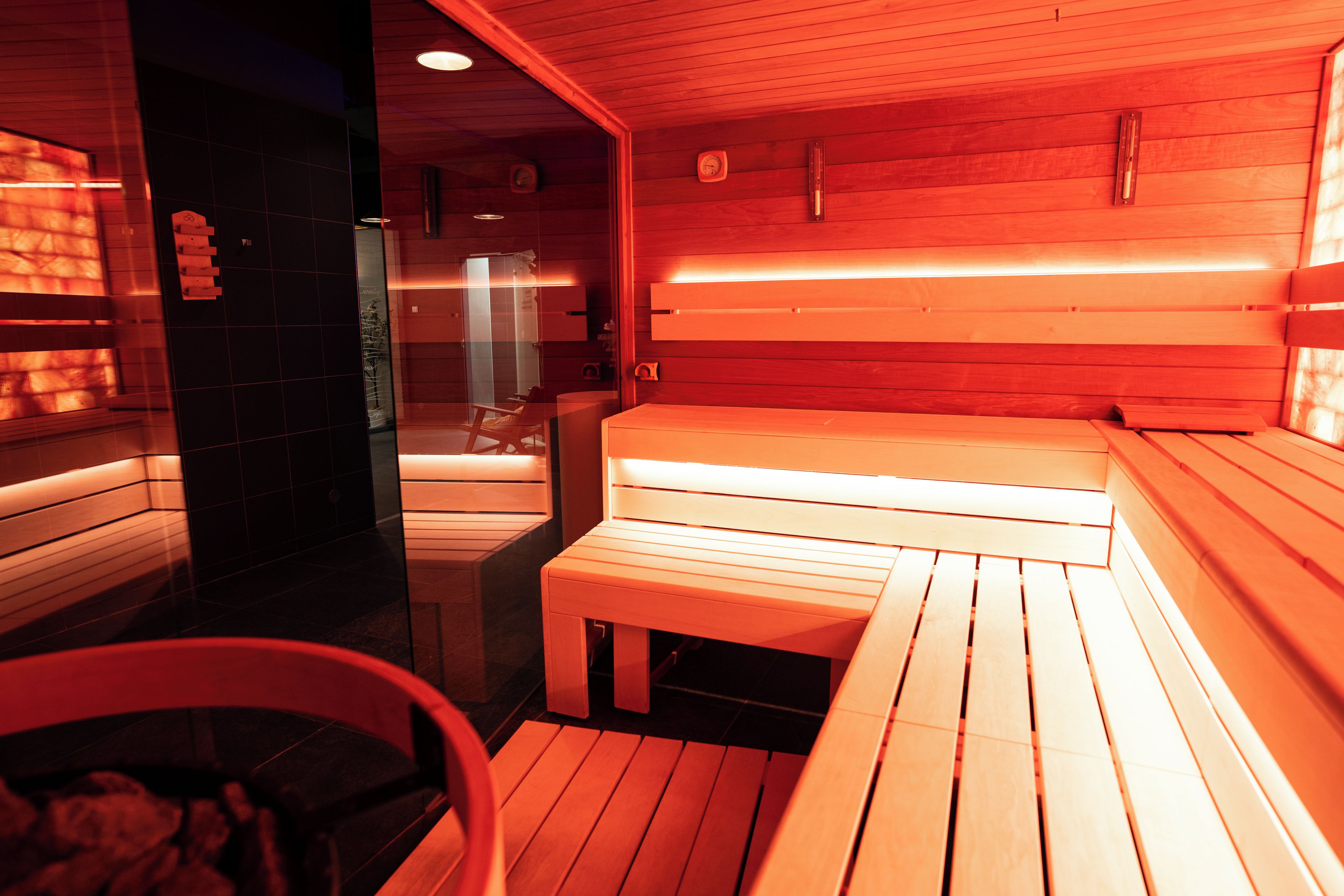Un sauna avec des bancs en bois et une porte en verre donnant sur un espace douche.