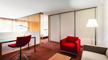 Una habitación de hotel moderna con un escritorio, una silla roja, un sofá y una lámpara.