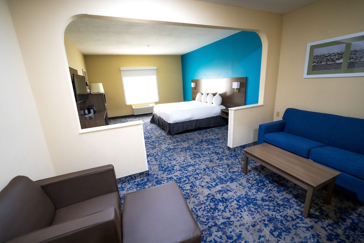A hotel room with a bed, a blue sofa, a small table, and a desk with a lamp.