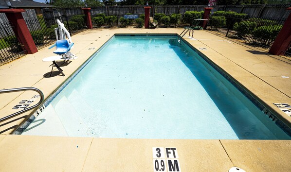 A rectangular swimming pool with a 3 FT 0.9 M depth marking, surrounded by a wooden fence, a lifeguard chair, and a lounge chair.