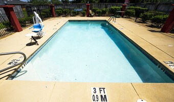 A rectangular swimming pool with a 3 FT 0.9 M depth marking, surrounded by a wooden fence, a lifeguard chair, and a lounge chair.