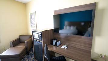 Una habitación de hotel con una cama, un escritorio, una silla, un televisor y un microondas.
