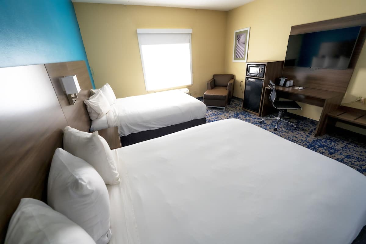 A hotel room with two beds, a desk, a chair, a television, and a microwave.