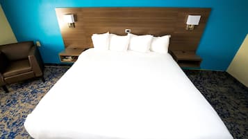 A hotel room with a large bed, two bedside tables, a chair, and a headboard with wall-mounted lamps.