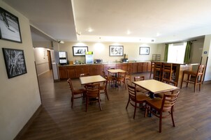 Un comedor amplio con mesas y sillas de madera, una cocina al fondo y obras de arte enmarcadas en las paredes.