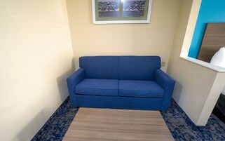 Un sofá azul en un rincón de una habitación, con un tapete estampado y un cuadro en la pared.