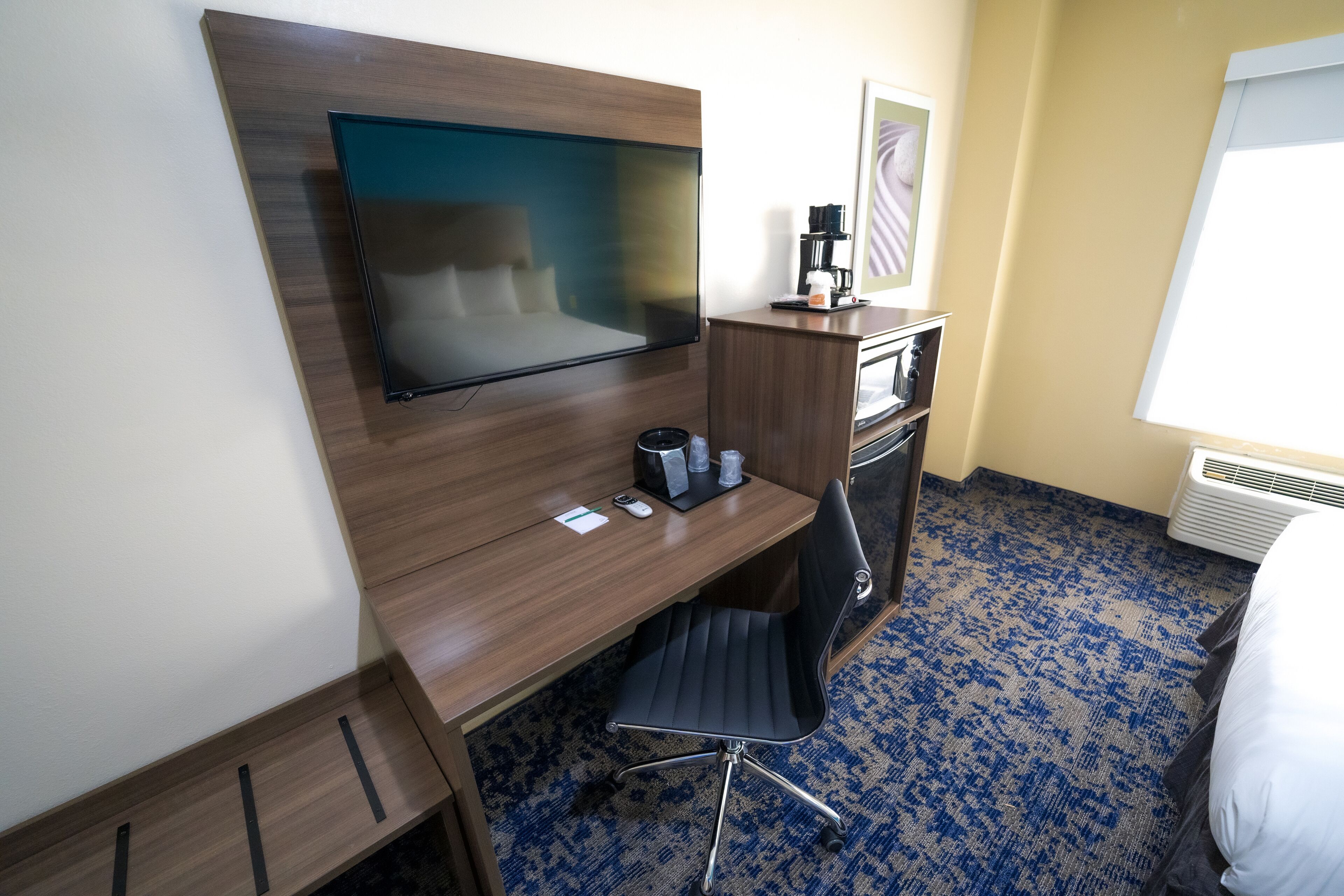 A hotel room with a wooden desk, a flat-screen TV, a coffee maker, and a chair.