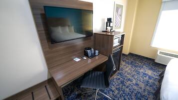 A hotel room with a wooden desk, a flat-screen TV, a coffee maker, and a chair.