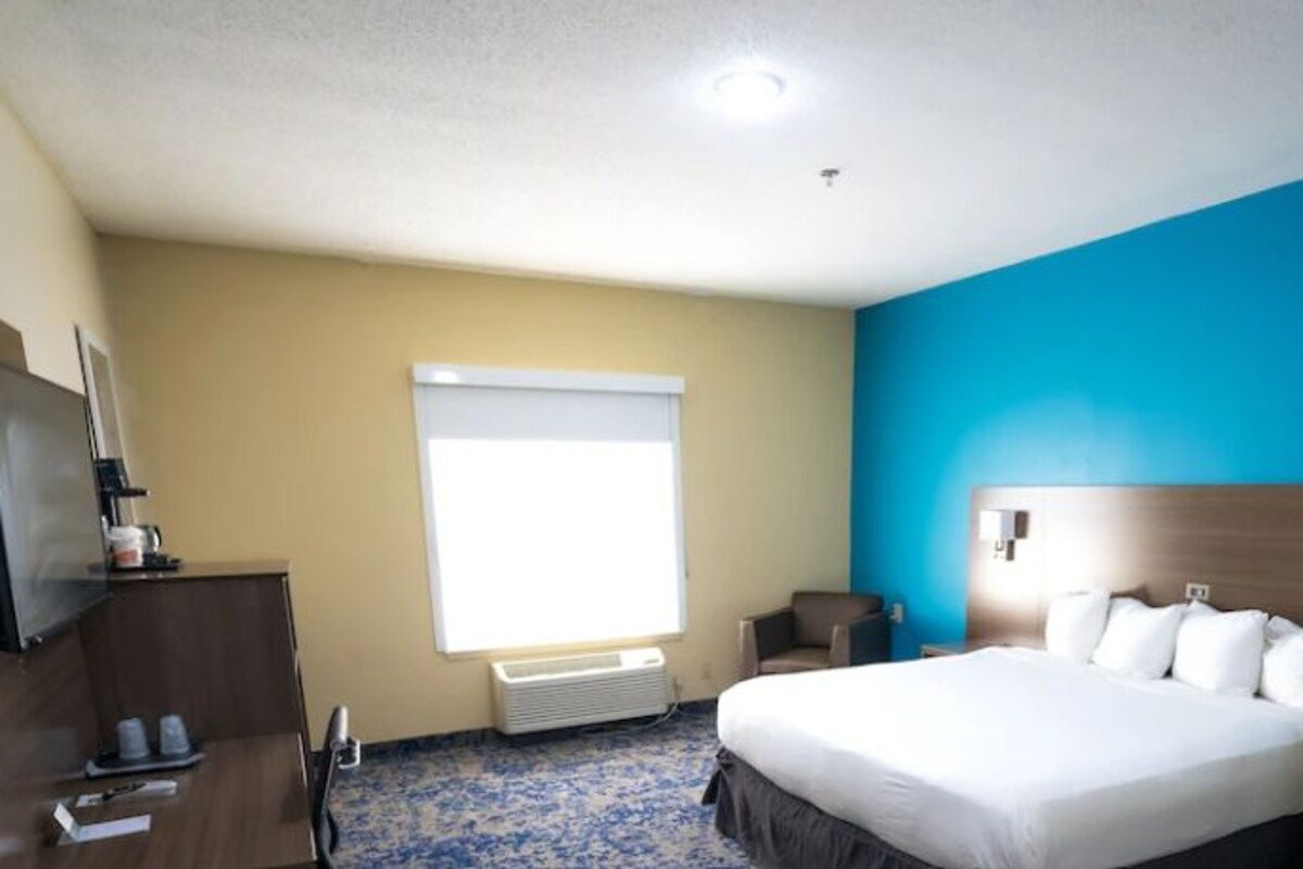 Habitación de hotel con cama, mesita de noche, televisión y ventana con persianas.
