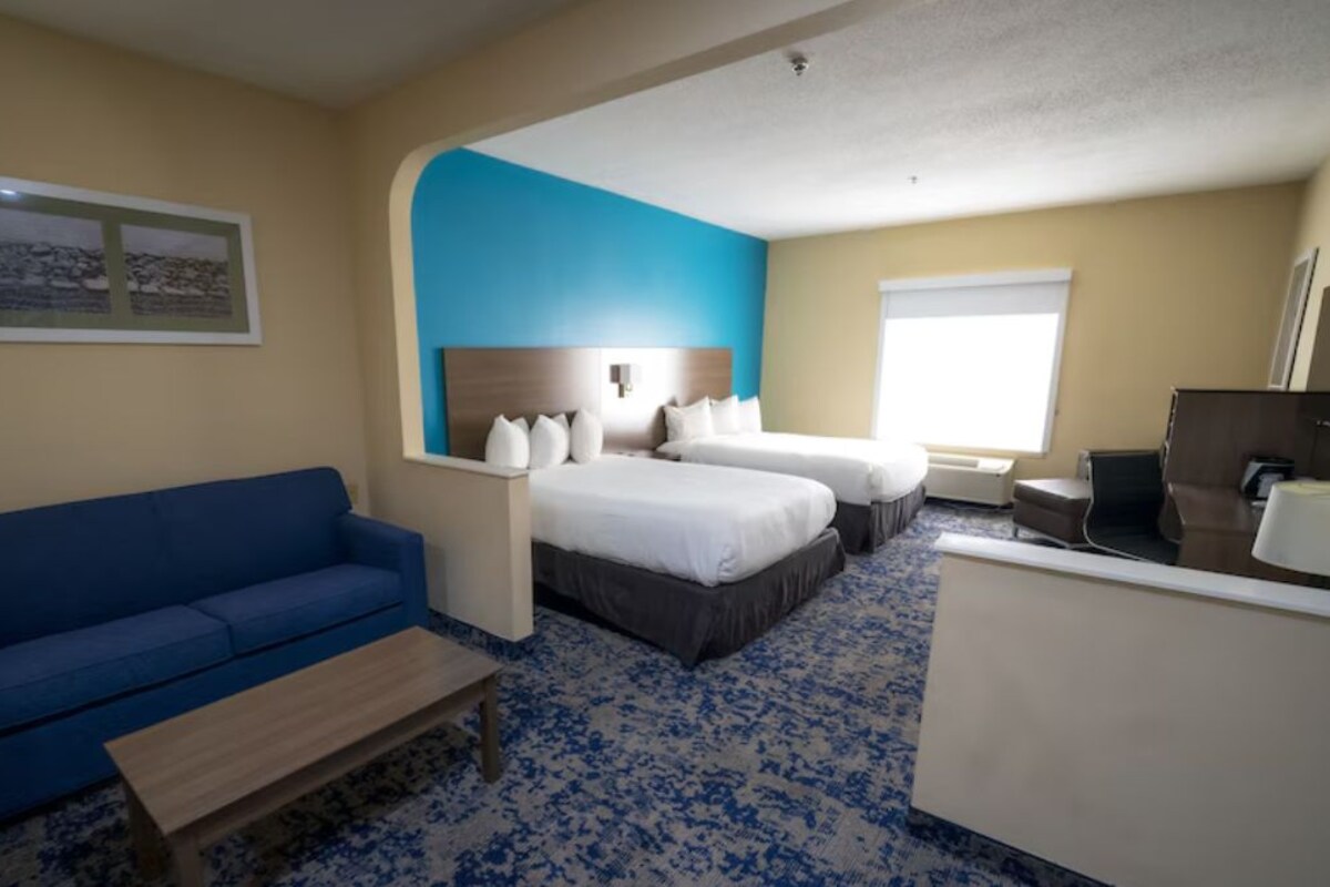 Una habitación de hotel con un sofá azul, dos camas, un escritorio y una ventana.