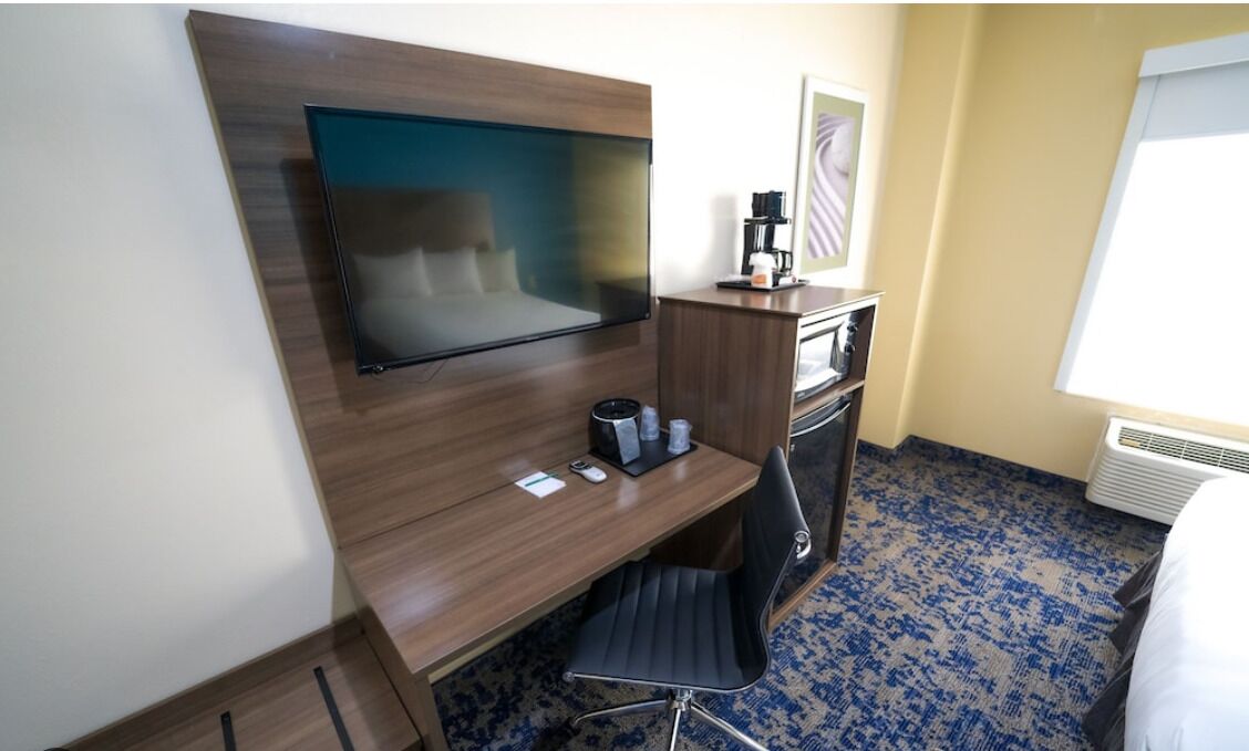 Habitación de hotel con televisor de pantalla plana montado en una pared de madera, un escritorio con una silla, una cafetera y una mesita con tazas.