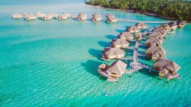 An aerial view of overwater bungalows connected by walkways over turquoise waters. - Le Taha'a by Pearl Resorts (Taha'a)