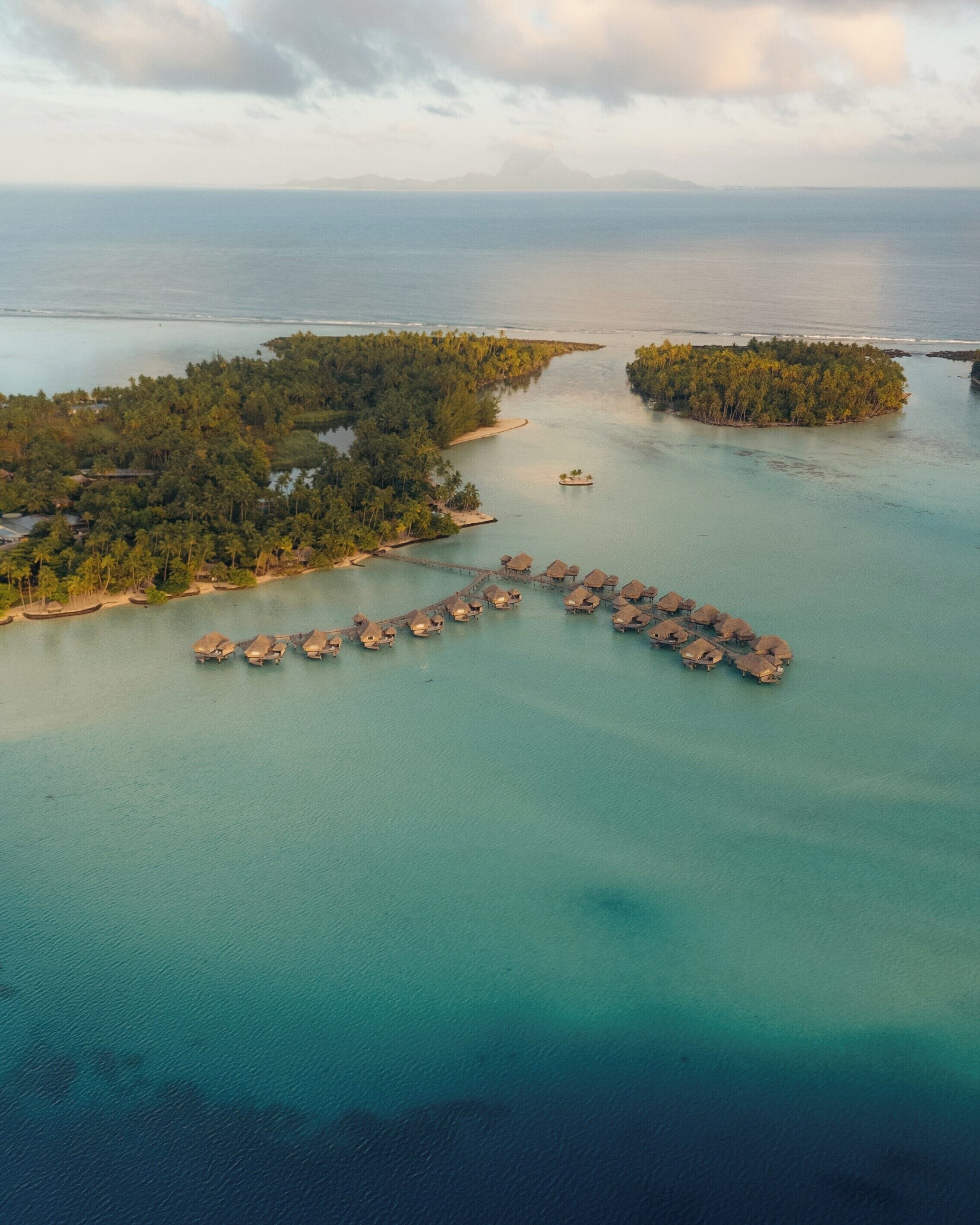 Vista aerea di un'isola resort con bungalow sull'acqua collegati da un pontile.