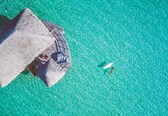 An aerial view of a beach with a thatched-roof structure and a clear turquoise sea.