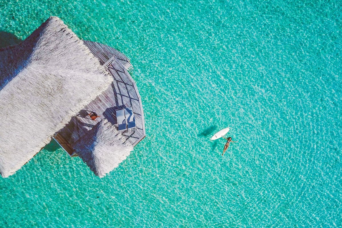 An aerial view of a beach with a thatched-roof structure and a clear turquoise sea.