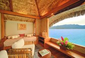 A room with a bed, a sofa, a small table, and a view of the sea.