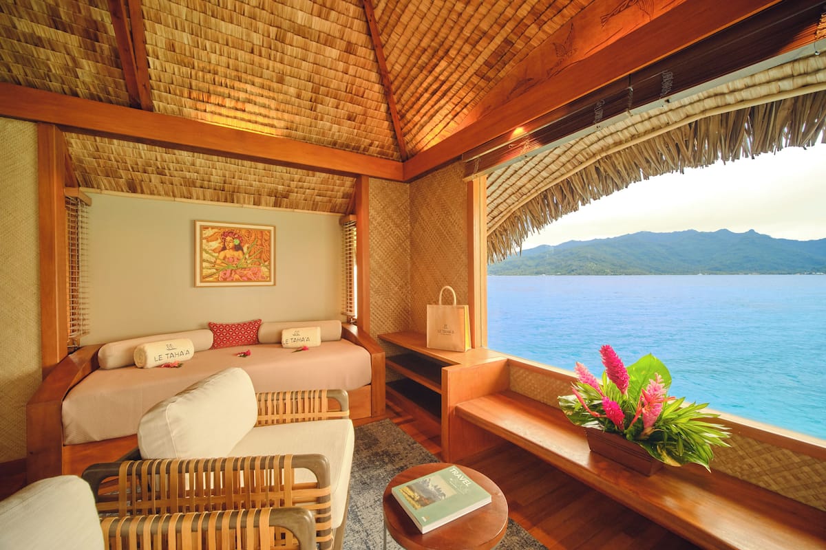 A room with a bed, a sofa, a small table, and a view of the sea.