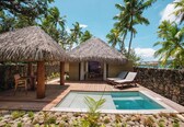 A pool area with thatched umbrellas, lounge chairs, and a stone wall.