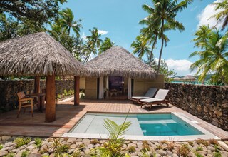 A pool area with thatched umbrellas, lounge chairs, and a stone wall.