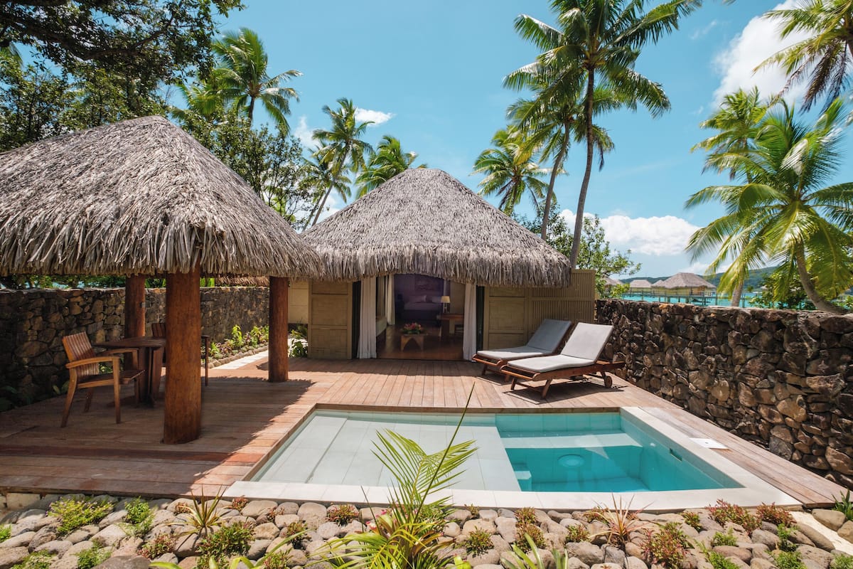 A pool area with thatched umbrellas, lounge chairs, and a stone wall.