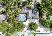 An aerial view of a resort with a swimming pool, thatched-roof structures, and lush greenery.