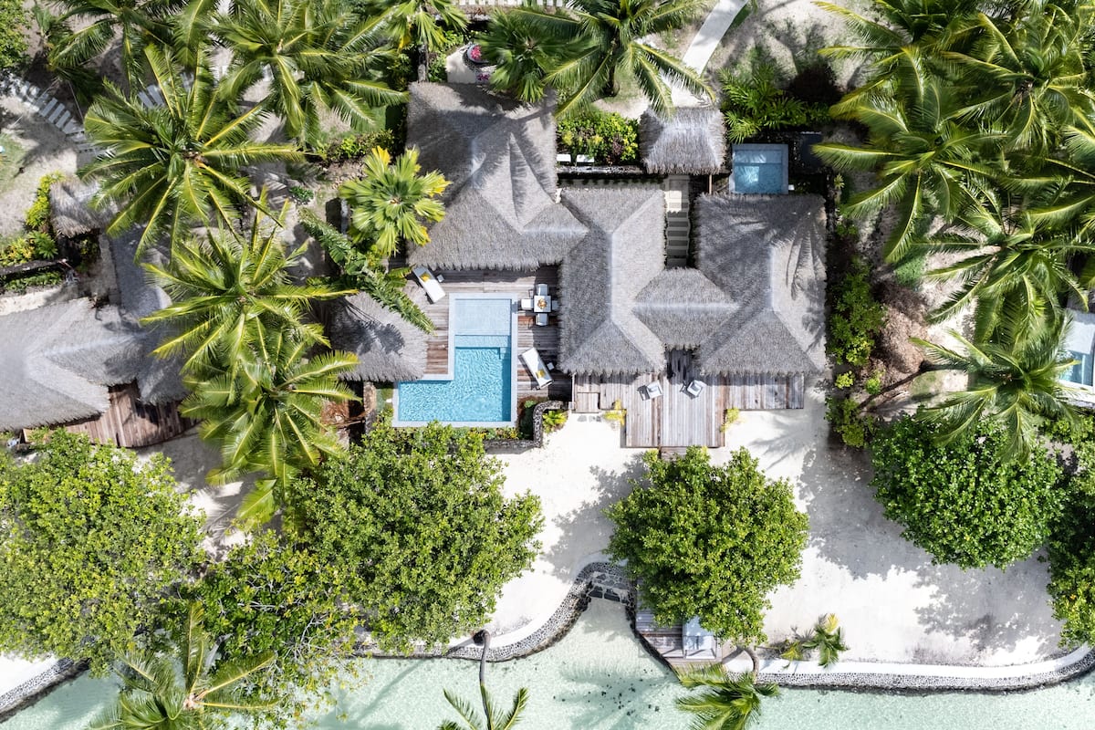 An aerial view of a resort with a swimming pool, thatched-roof structures, and lush greenery.