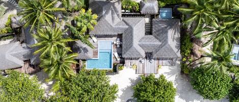 An aerial view of a resort with a swimming pool, thatched-roof structures, and lush greenery.