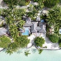 Vista aérea de un resort con piscina, construcciones de techo de paja y exuberante vegetación.
