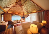 A hotel room with a large bed, a sitting area, a TV, and a view of the sea.