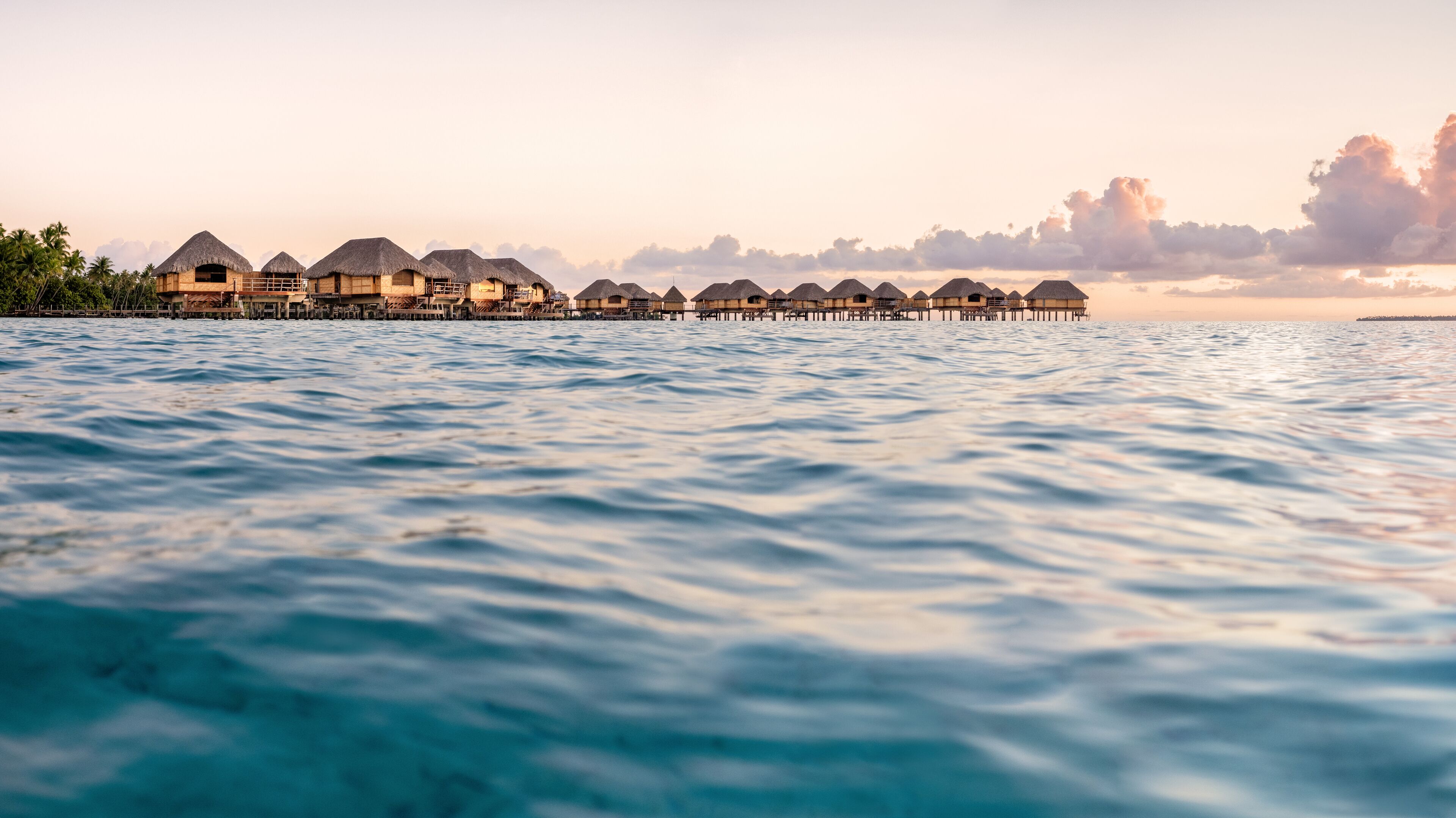Overwater bungalows with thatched roofs, connected by walkways over calm water.