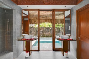 A modern bathroom with two sinks, a shower, and a view of a pool and garden.