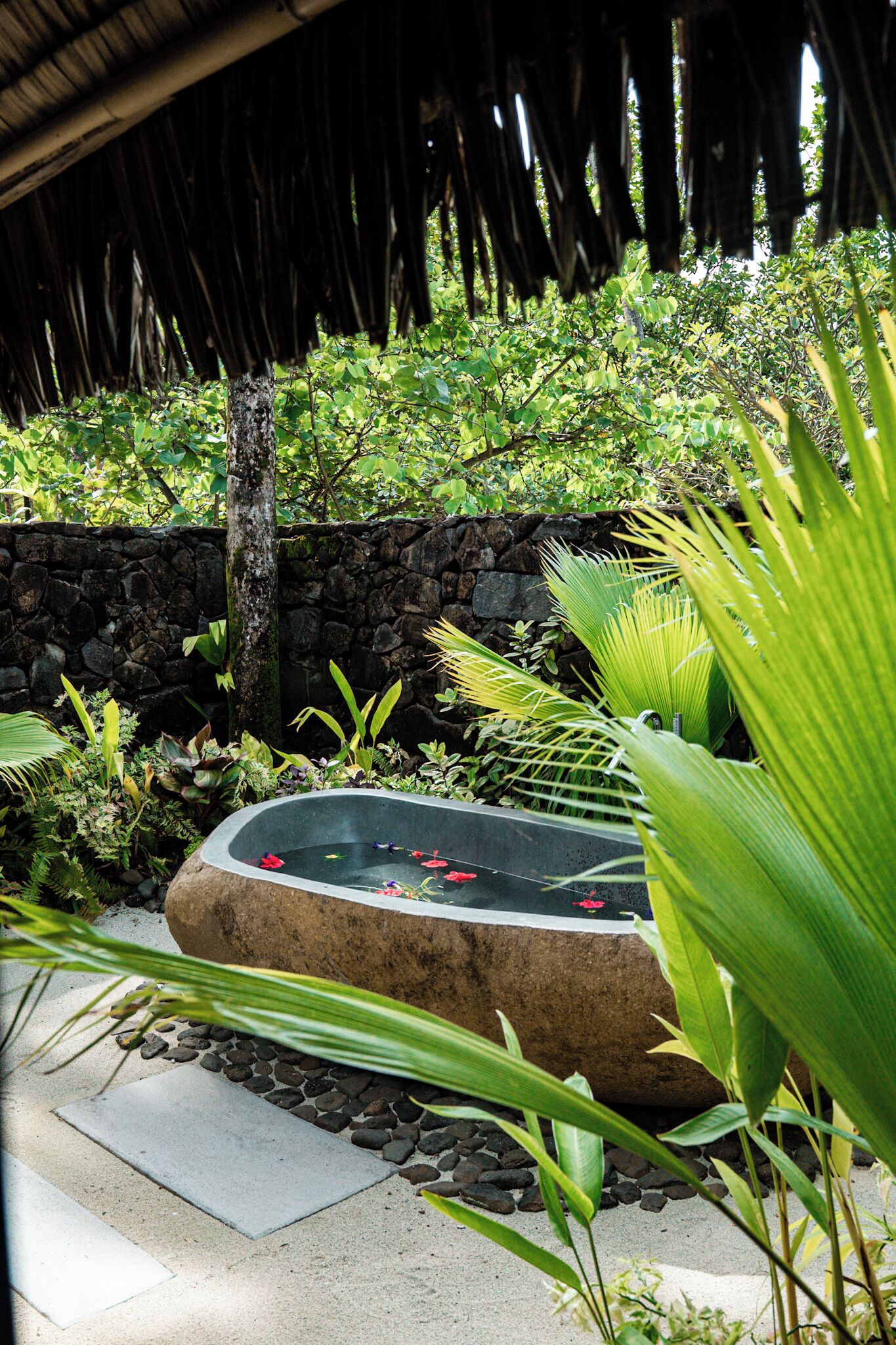 A stone wall, a thatched roof, and a water feature with rocks and plants.
