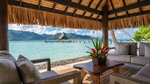 A wooden deck with a thatched roof overlooking turquoise waters and a mountain range. - Le Taha'a by Pearl Resorts (Taha'a)