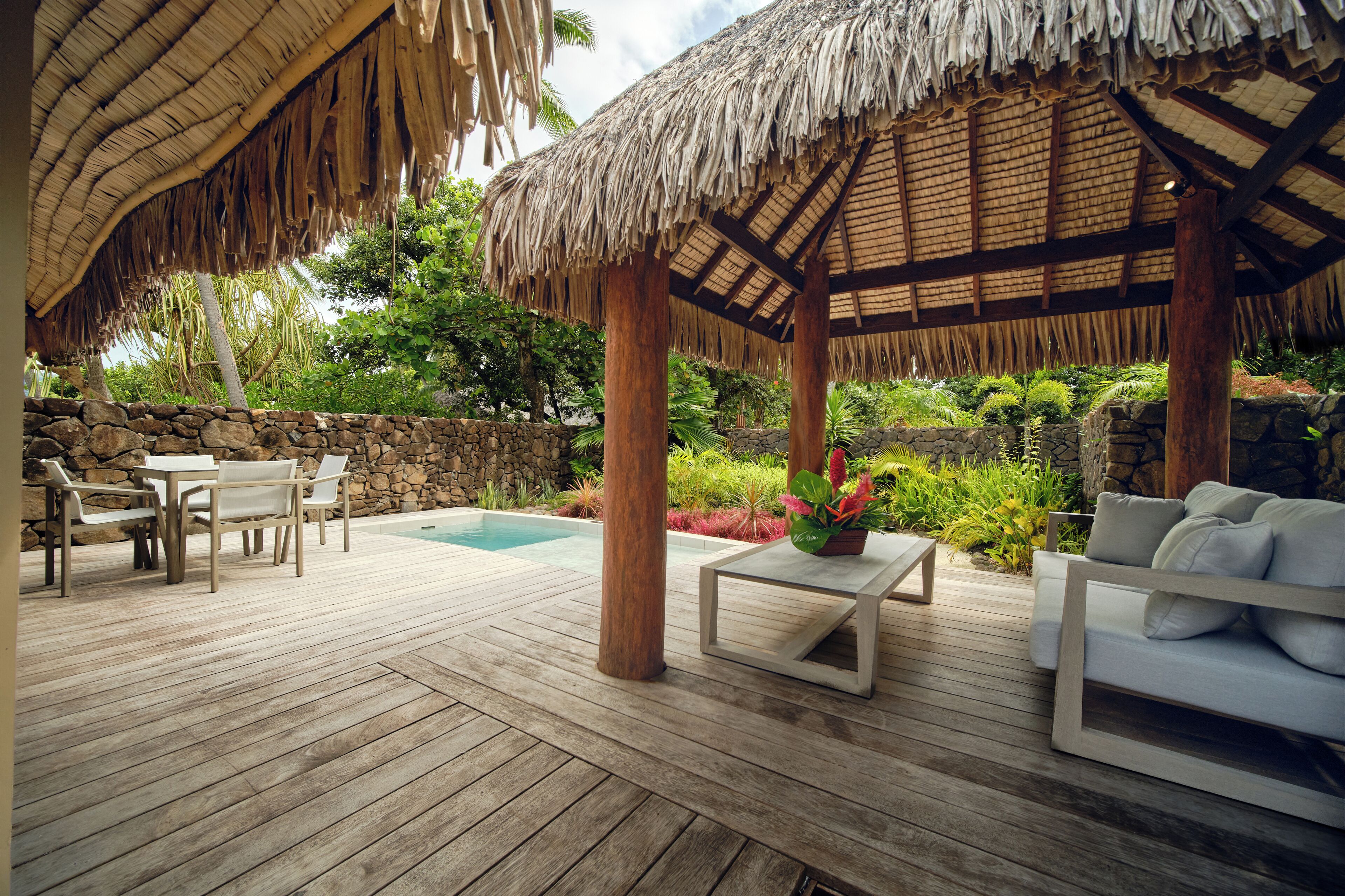 Una terraza de madera con techo de paja, una piscina y mobiliario exterior.