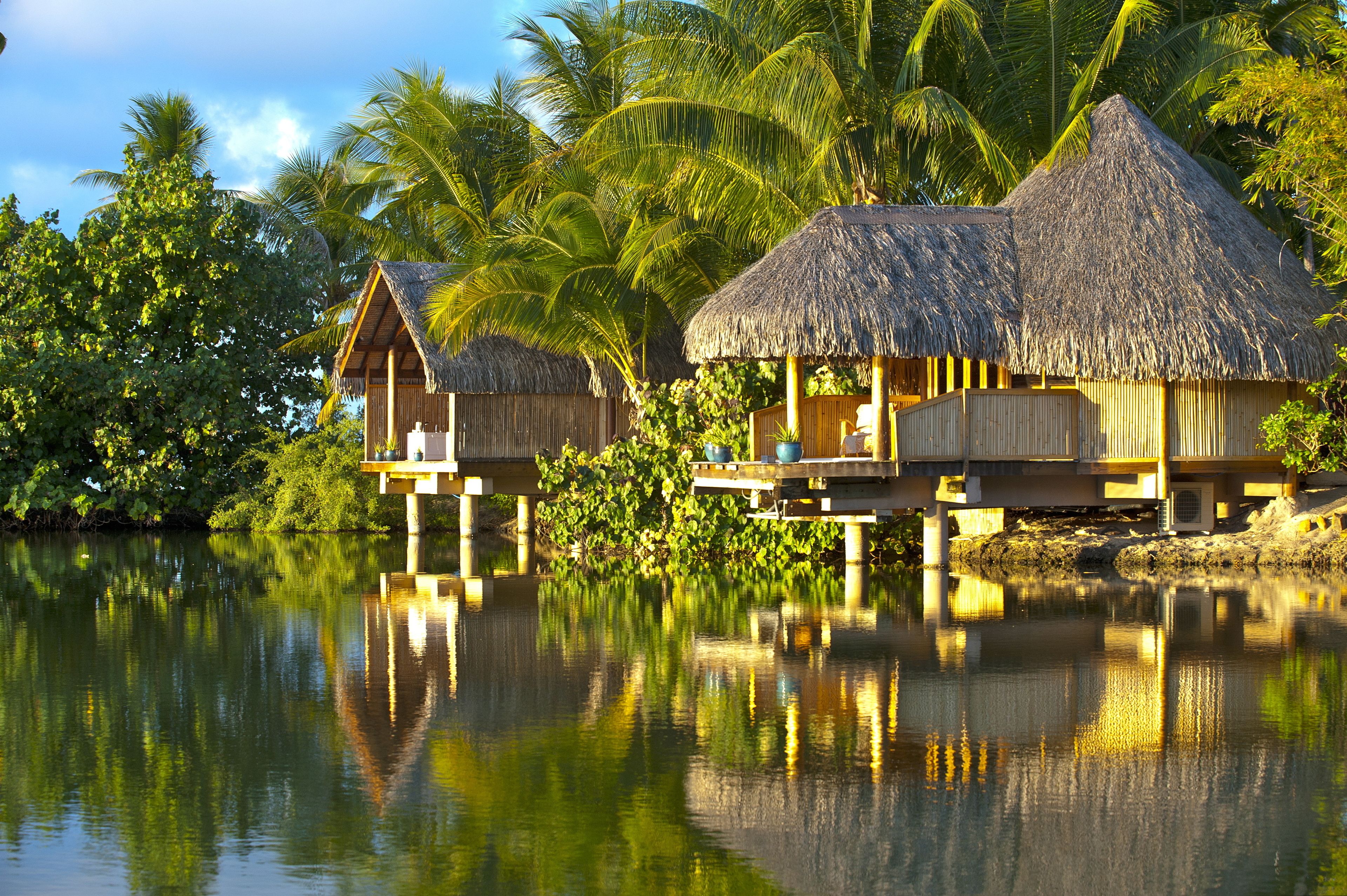 Overwater bungalows with thatched roofs, wooden railings, and a calm water body reflecting the structures.