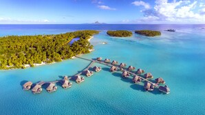 An aerial view of a tropical island resort with overwater bungalows connected by a bridge, surrounded by clear turquoise waters and lush greenery. - Le Taha'a by Pearl Resorts (Taha'a)