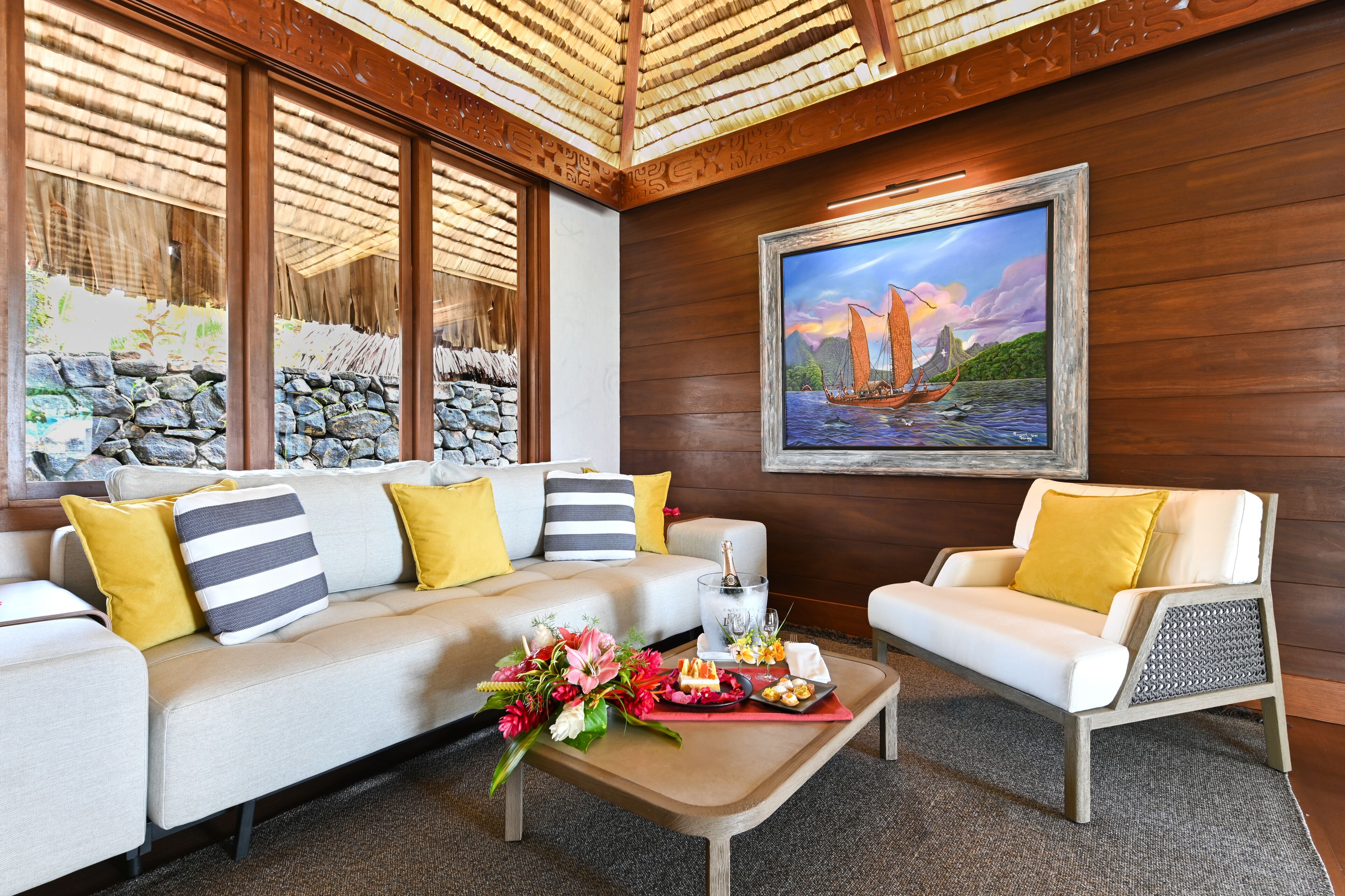 Una sala de estar moderna con sofá, sillón y mesa de centro. Hay un cuadro en la pared y una ventana con vistas a un paisaje rocoso.
