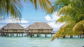 Overwater bungalows with thatched roofs, connected by walkways, in a clear blue sea.