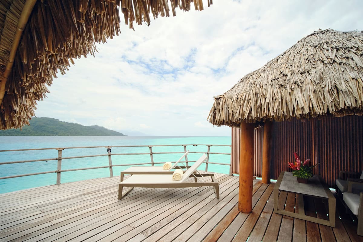 A wooden deck with a lounge chair and a table, overlooking turquoise waters and a distant island.