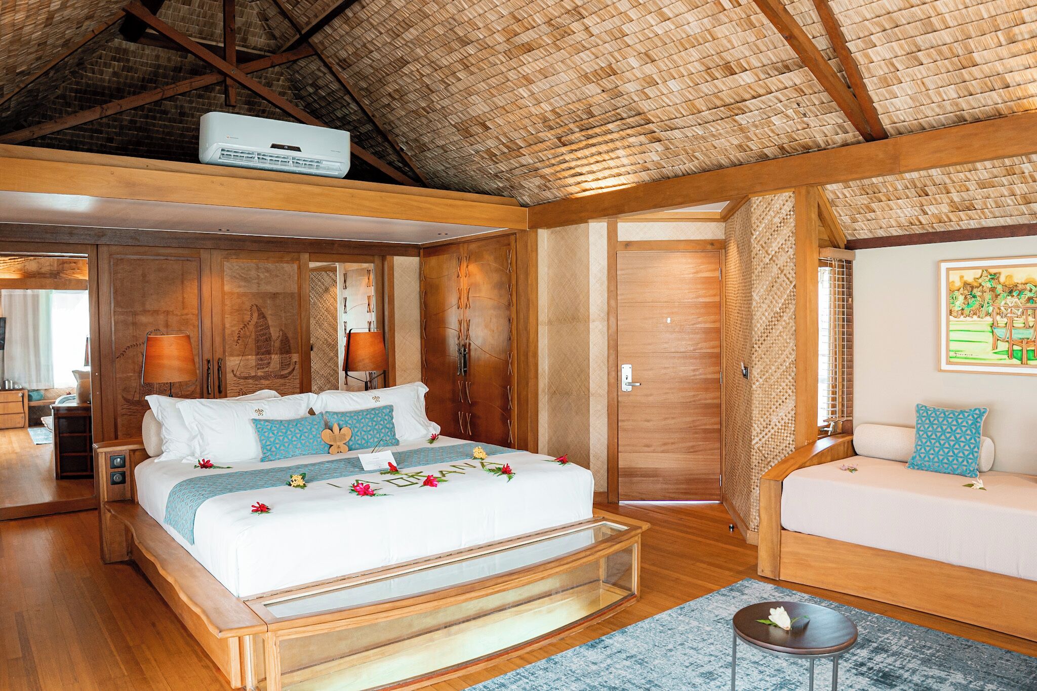 A spacious bedroom with a large bed, a wooden bench, a sofa, and a ceiling fan.