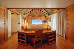A room with a wooden desk, two chairs, a TV, and a view of the sea.