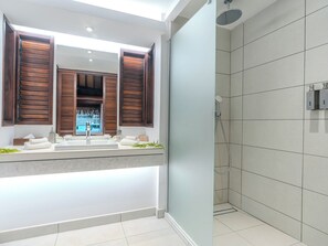 A modern bathroom with a large mirror, wooden shutters, a shower, and a tiled floor.