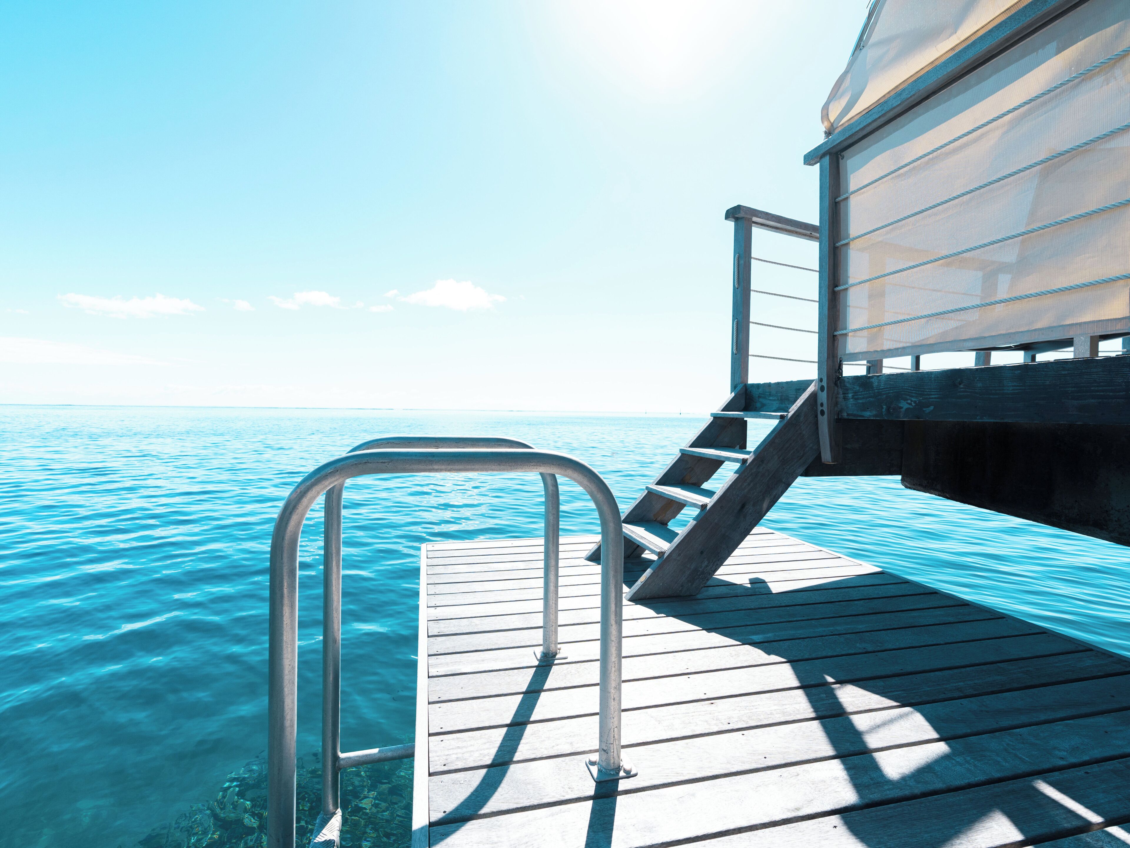 A wooden deck extending over water with a metal railing and stairs leading to a covered area.