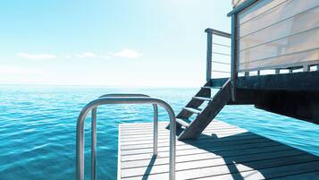 A wooden deck extending over water with a metal railing and stairs leading to a covered area.