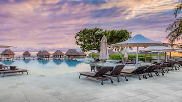 A poolside area with lounge chairs, umbrellas, and overwater bungalows.